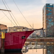 Historisches rotes Schiff im Bremer Hafen vor moderner Stadtkulisse am Wasser als Key Visual für das BOEHMERT & BOEHMERT IP-Seminar in Bremen