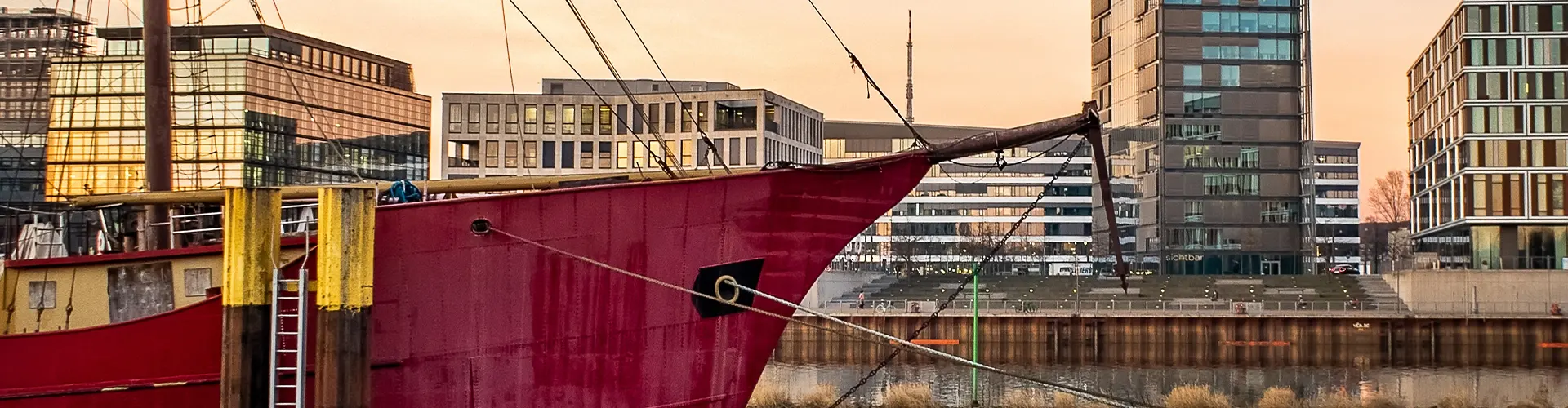 IP-Seminar Bremen, BOEHMERT & BOEHMERT Historisches rotes Schiff im Bremer Hafen vor moderner Stadtkulisse am Wasser als Key Visual für das BOEHMERT & BOEHMERT IP-Seminar in Bremen