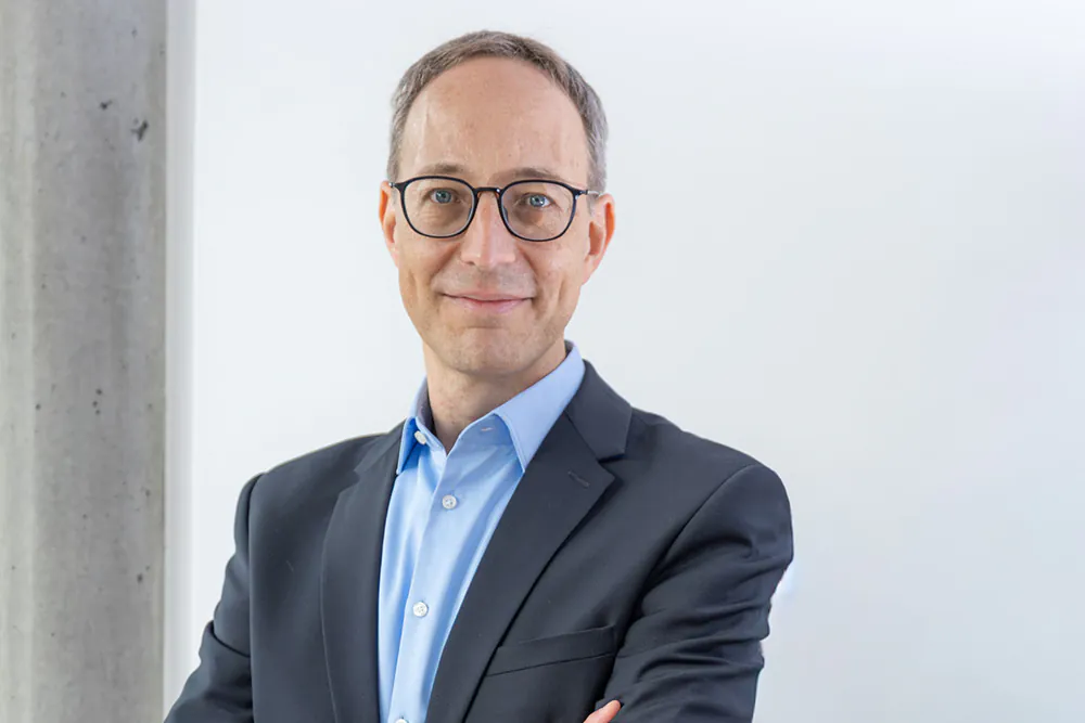 Portraitfoto des European Patent Attorney Théodore Ley, der bei BOEHMERT & BOEHMERT in München arbeitet, einen dunklen Anzug und ein hellblaues Hemd trägt und in die Kamera lächelt.